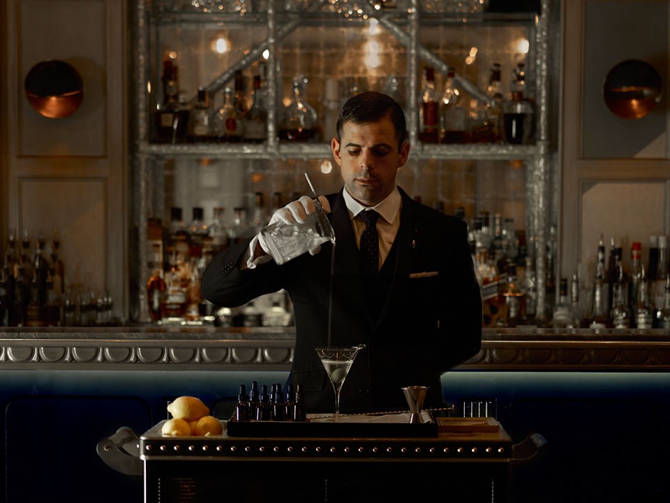 A focused mixologist who, after preparing a drink, pours it into a martini glass.