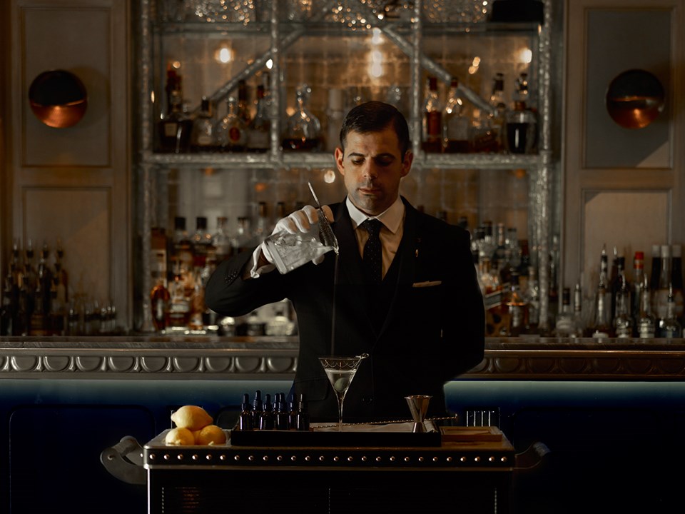 A focused mixologist who, after preparing a drink, pours it into a martini glass.