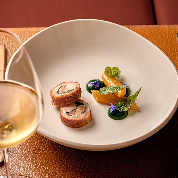 an artfully plated dish of roulade, accompanied by vibrant vegetables and herbs, complemented by a glass of white wine.