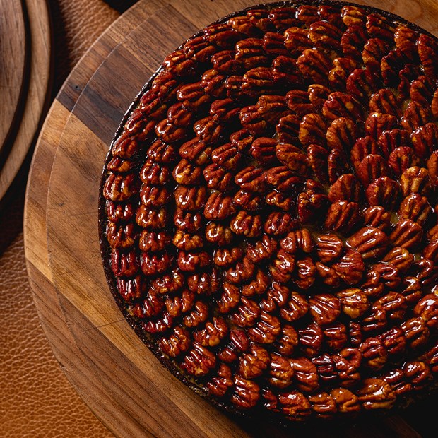 A meticulously arranged pecan tart with a glossy glaze, highlighting the rich, warm tones of the pecans against a wooden backdrop.