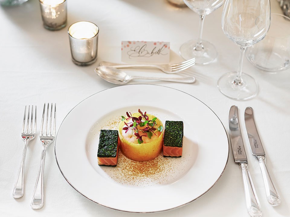 Presentation of a delicious salmon dish on a white plate, with escaige and candles at The Connaught.