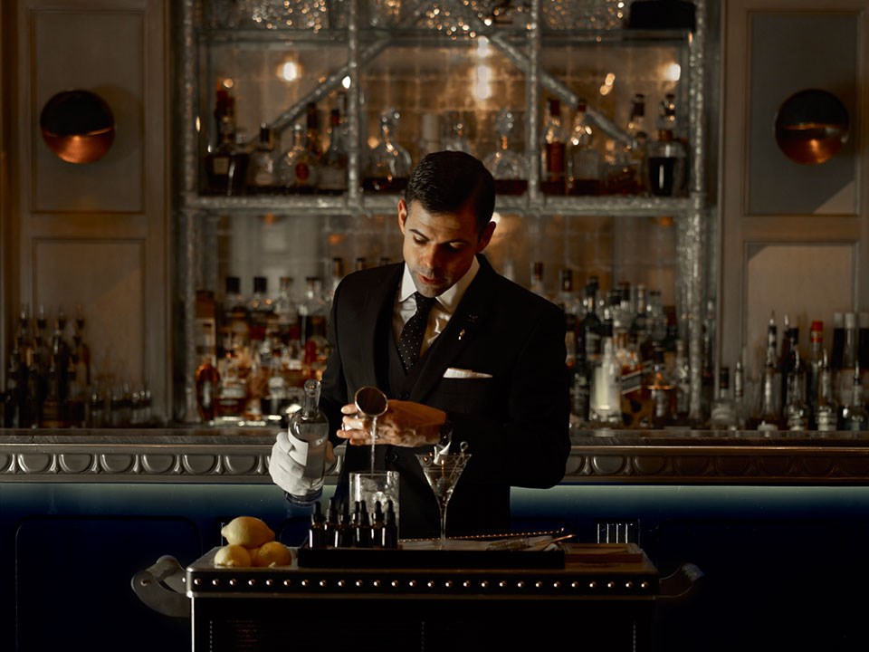 A depiction of a sophisticated bartender making a cocktail at the bar at The Connaught.
