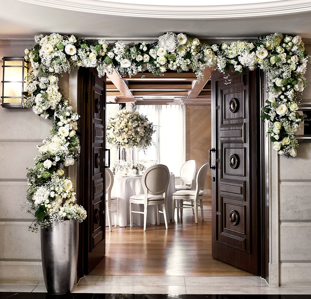 The Maple Room at The Connaught with beautiful flowers above the entrance door and a round table set up for a wedding reception