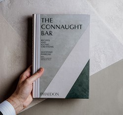 the connaught bar hardcover book held by man in front of grey background
