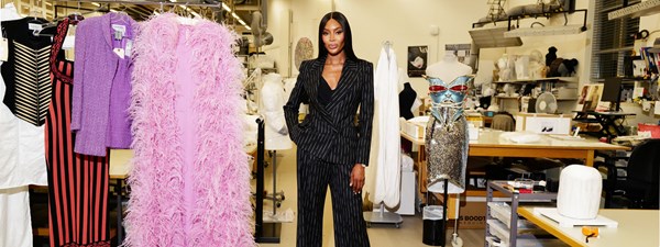 Naomi in pin striped suite in an atelier with clothes around her