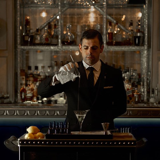 A focused mixologist who, after preparing a drink, pours it into a martini glass.