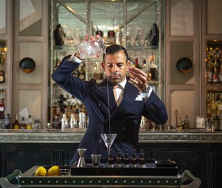 A focused mixologist pours a drink into a martini glass in the interior of The Connaught Bar.