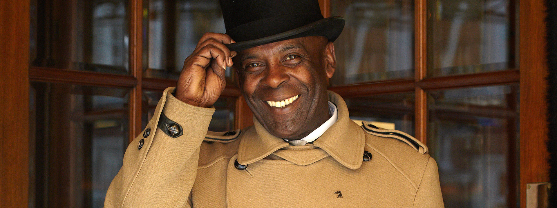 A smiling man clutching his hat.