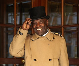 Portrait of a smiling doorman with a hat in front of a hotel, greeting his guests.