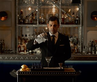 A focused mixologist who, after preparing a drink, pours it into a martini glass.