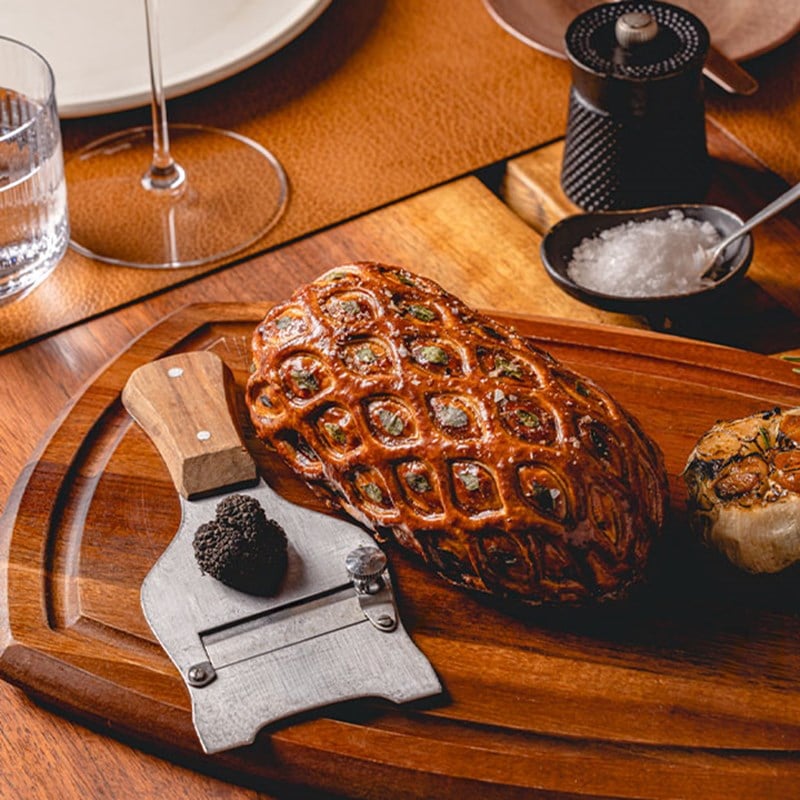 A meticulously baked beef Wellington displayed on a wooden board with truffle and roasted garlic, ready to be served in a refined setting.