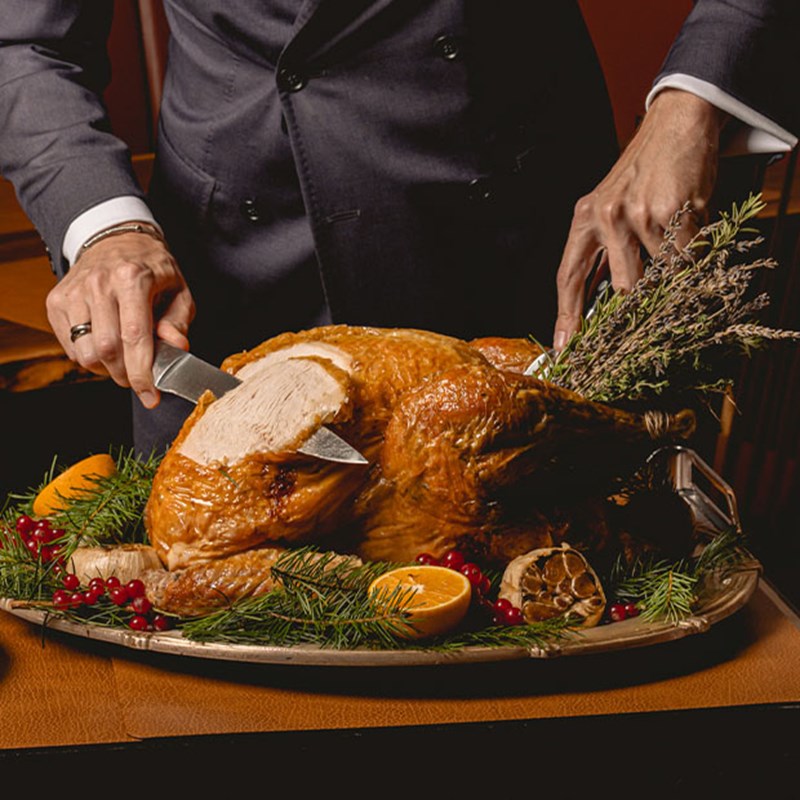 A traditional roast turkey being carved tableside, garnished with herbs, oranges, and cranberries for a festive touch.