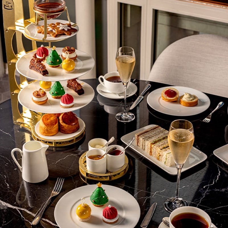 An elaborate afternoon tea spread with festive pastries, scones, finger sandwiches, and Champagne, elegantly arranged on a multi-tiered stand for a luxurious seasonal treat.