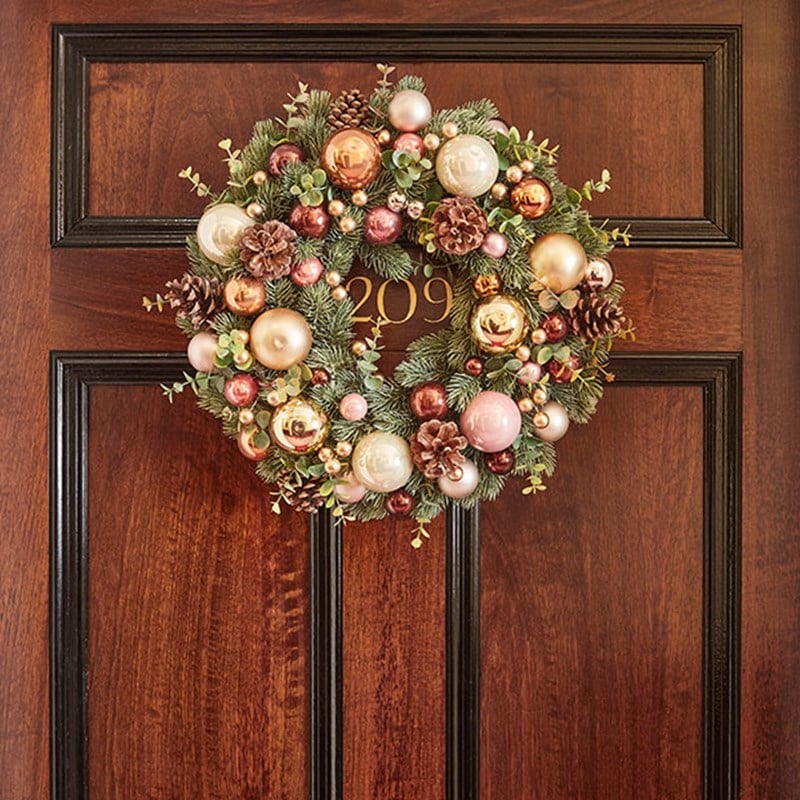 Wreath on a wooden suite door, decorated with baubles and pine cones.