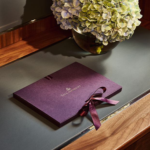 Purple Connaught gift envelope tied with ribbon, placed on a wooden desk beside a vase of hydrangeas.