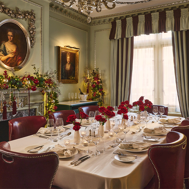 Elegant Georgian dining room with Christmas garlands and a white-clothed table set with red rose centrepieces