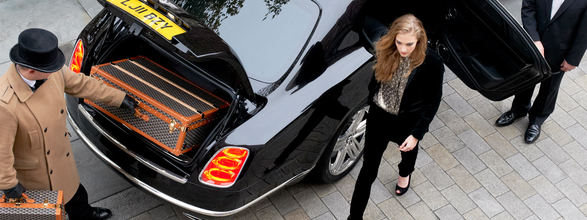 A person getting out of the car being accompanied by a driver and a concierge helping with the suitcase.