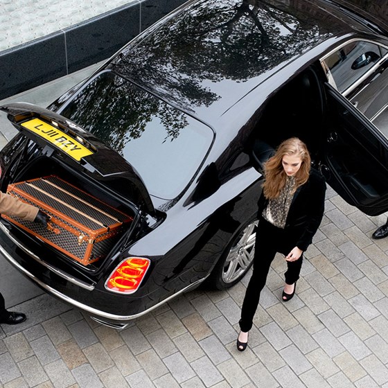 A concierge taking travel bags out of a car, and an incoming hotel guest stepping from the car.