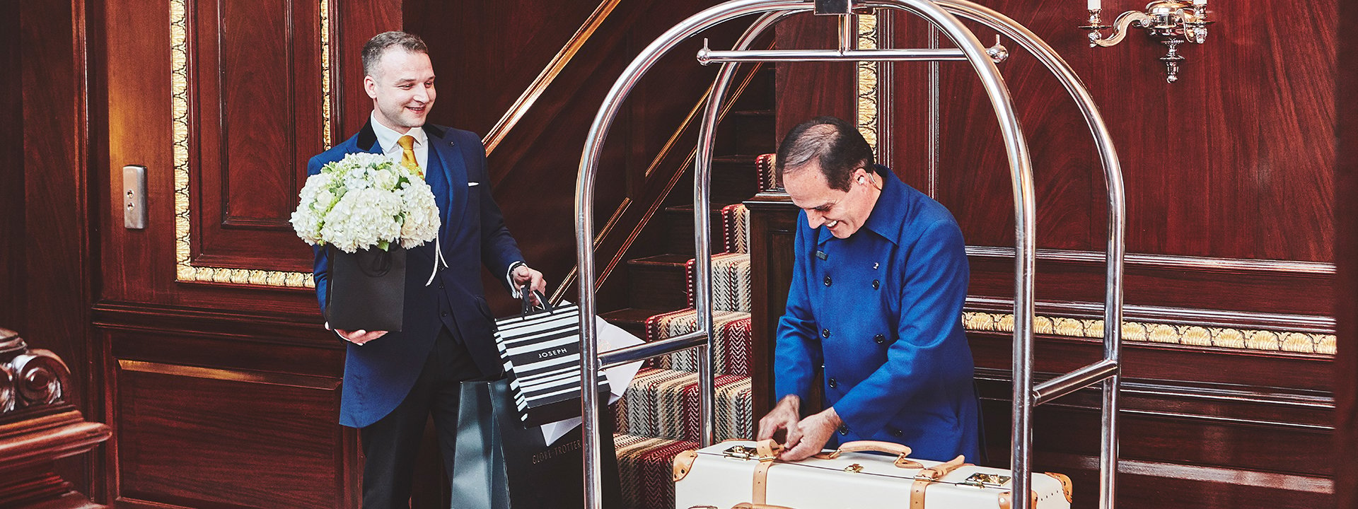 The concierge team, one man handling the luggage and the other is holding a bouquet of flowers.