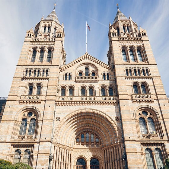 View of the front of the National History Museum, an impressive building with blue sky in the background.