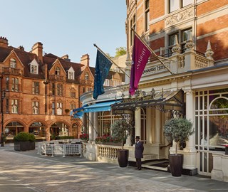 Exterior view of The Connaught Hotel with flags, a doorman at the entrance, and surrounding historic buildings in daylight.