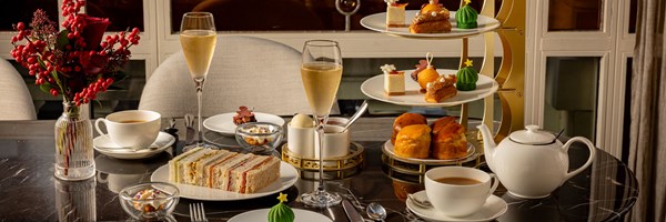 Wide view of the tea table, tiered stand, teapot, champagne glasses and floral arrangement.