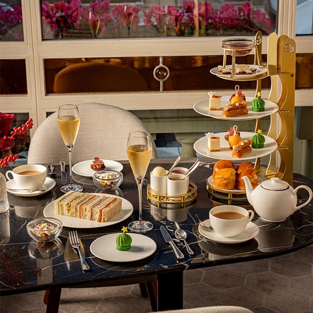 Elegant afternoon tea table with tiered pastries, sandwiches, scones, champagne and tea by a window.