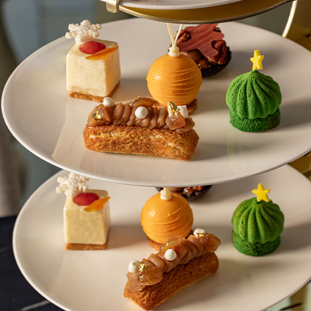 Plates of festive pastries, including an orange sphere, green dome and vanilla square, arranged on tiered stands.