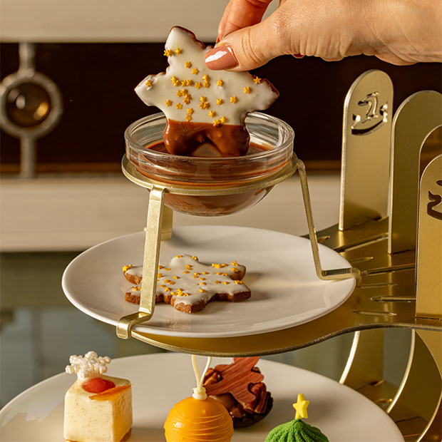 Hand dipping a star-shaped iced biscuit into a small bowl of chocolate sauce.