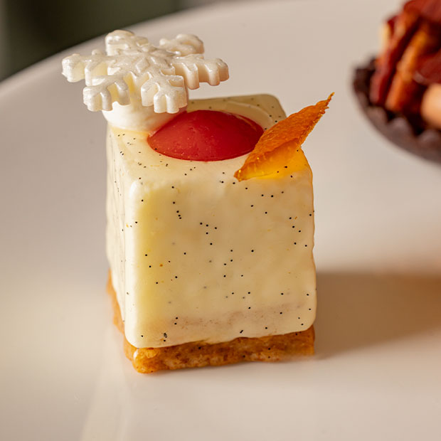 White vanilla mousse square topped with a sugar snowflake and red glaze accent.