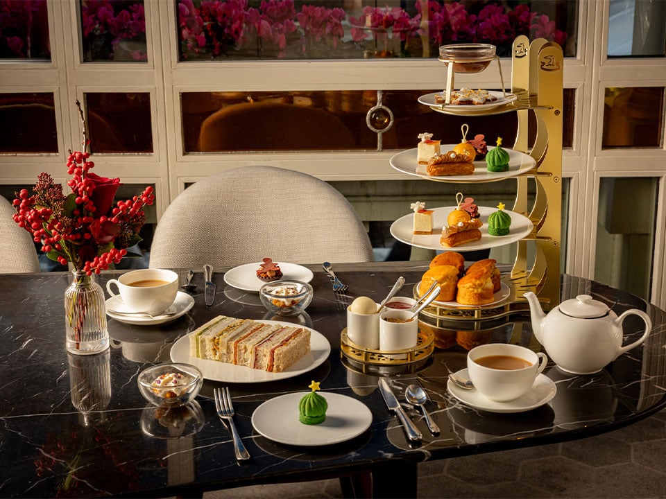 Afternoon tea spread with pastries, scones, sandwiches and champagne on a marble table.