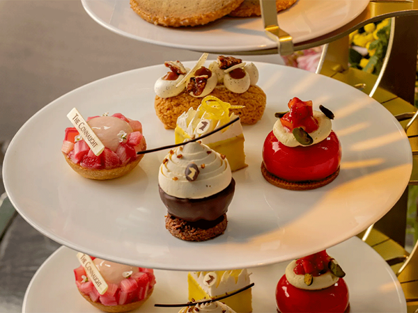 An elegant afternoon tea stand with assorted colourful pastries and mini cakes displayed on white tiered plates.