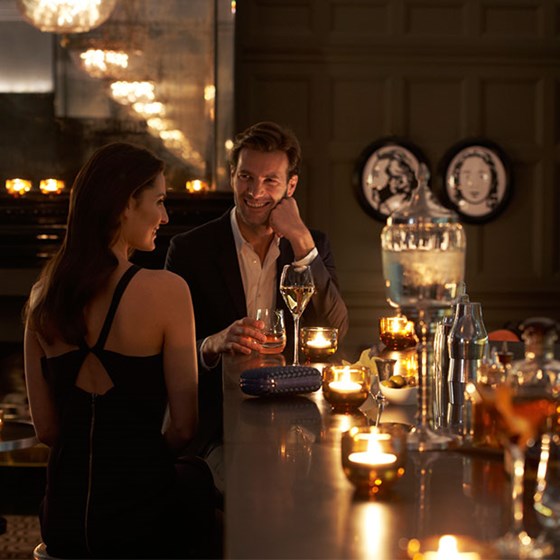 A smiling man and woman enjoying a drink and conversation at the Coburg Bar, The Connaught.