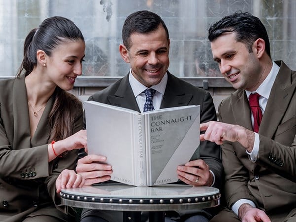 3 co authors of the Connaught Bar Cocktail book, smile as they browse through it