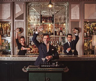 Three mixologists preparing drinks at The Connaught Bar, surrounded by the timeless elegance of the interior.