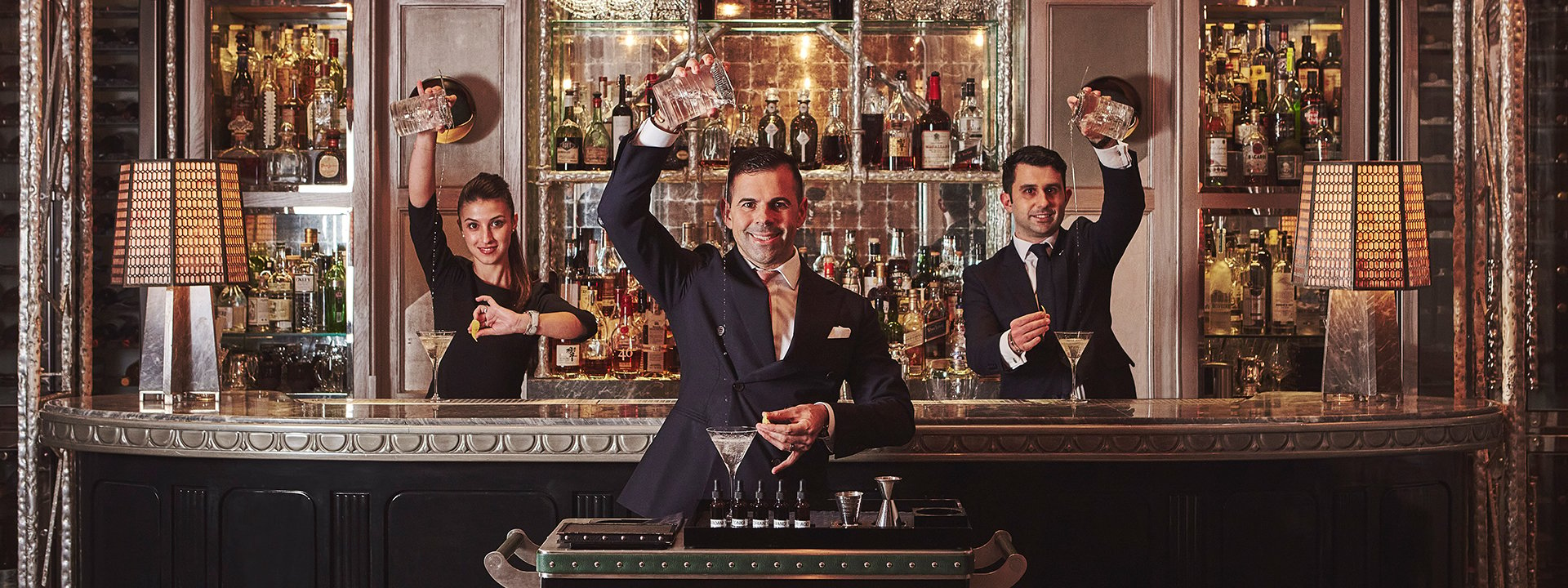 Three bartenders with their arms high up shaking a mixer.