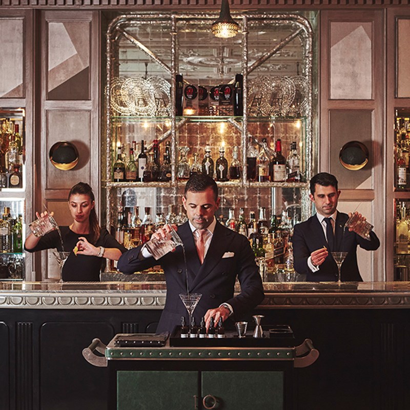 Three mixologists focus on preparing cocktails in the pleasant atmosphere of The Connaught Bar.