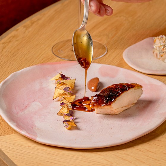 A delicious dish served on a pink plate, served and decorated with sauce and edible flowers.