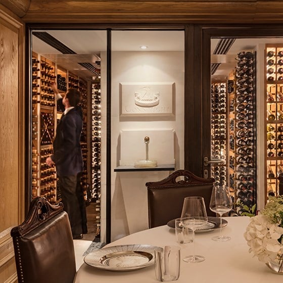 A part of the interior space with a rich wine collection, and a sommelier choosing wine at The Sommelier's Table.