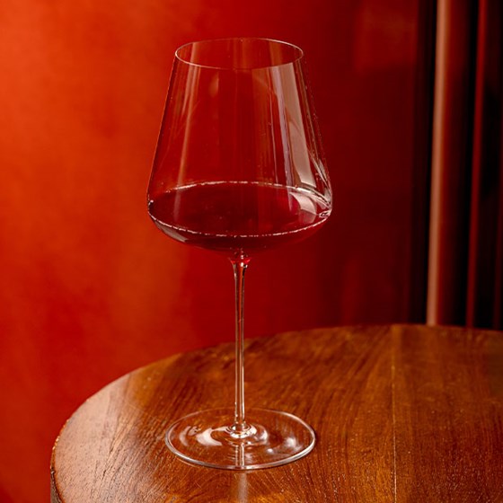 Elegant wine glass half-filled with red wine, placed on a polished wooden table against a rich red velvet backdrop.