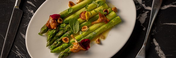 Warm asparagus spears with chanterelles, hazelnuts, and edible flowers on a white plate.