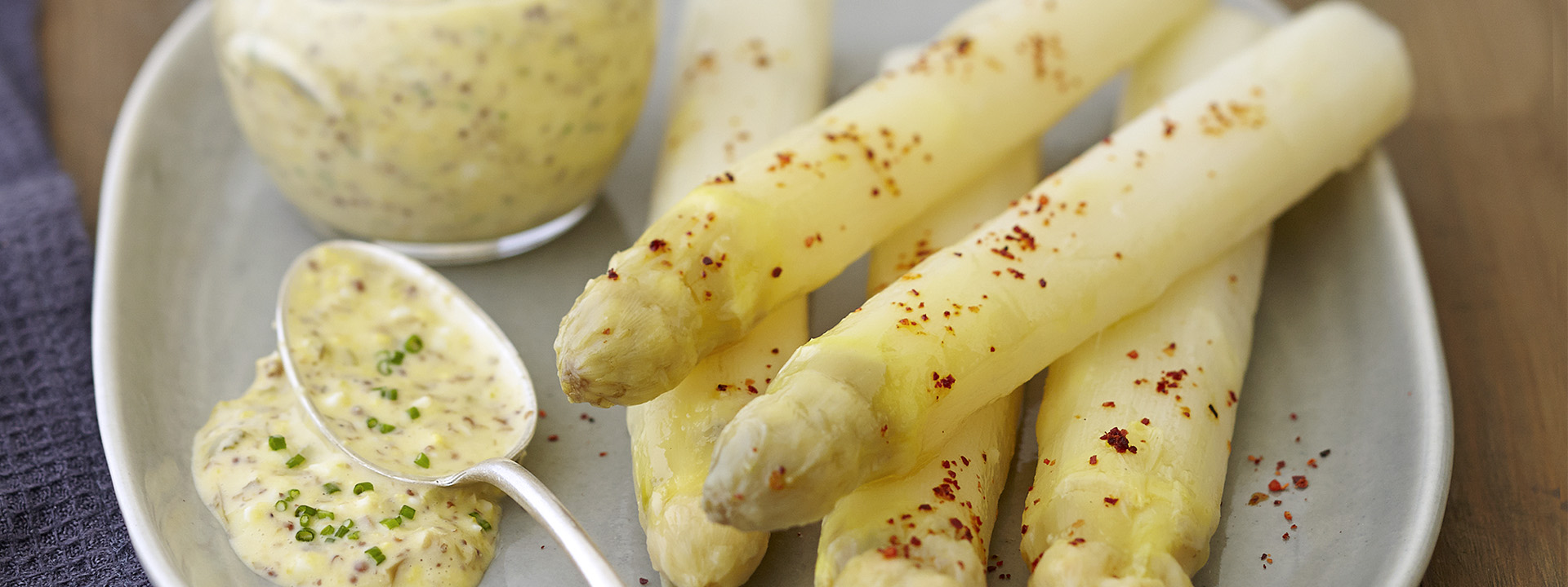 
Asparagus with spices and a spoon on a grey plate.