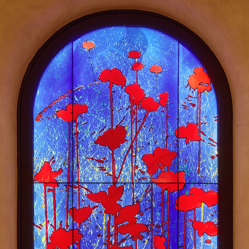 Close-up of an arched stained-glass window in The Red Room, adorned with vibrant red poppies against a deep electric blue background.