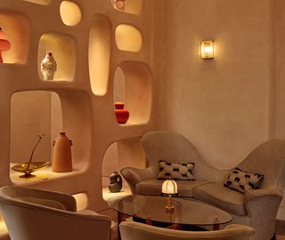 An intimate corner of the lounge with sculptural wall niches displaying curated ceramics, paired with a curved, textured loveseat and soft ambient lighting for a cosy, artful atmosphere.