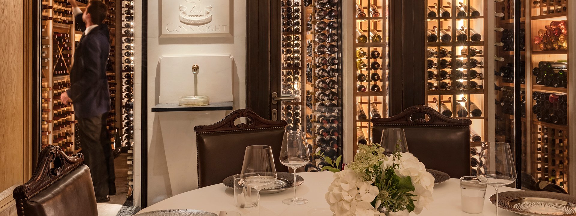 A table set in The Sommelier's Table, an atmospheric limestone wine cellar, surrounded by The Connaught's wine collection.