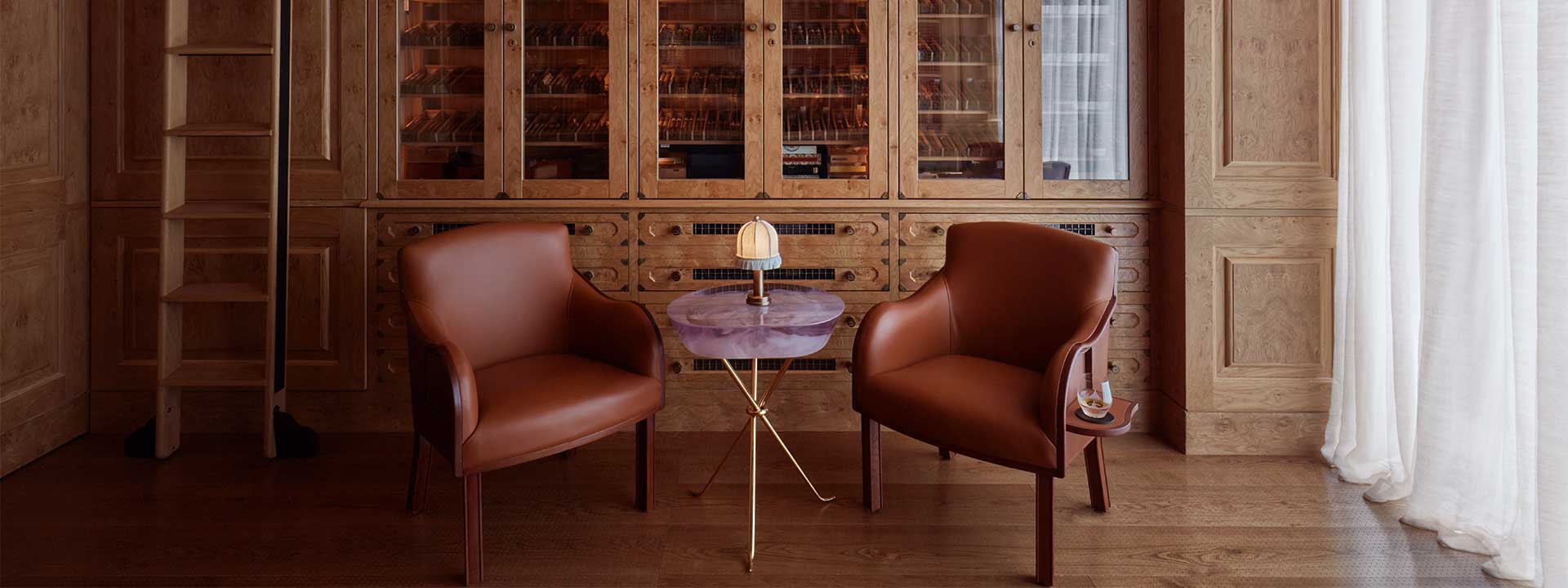 Two comfortable armchairs and a small table with a lamp in the warm interior of The Connaught Cigar Merchants.