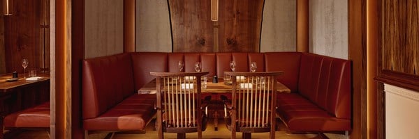 Corner banquette seating at The Connaught Grill, featuring curved leather upholstery in a rich sienna tone, natural wood details, and a softly illuminated, modern timber-lined interior.
