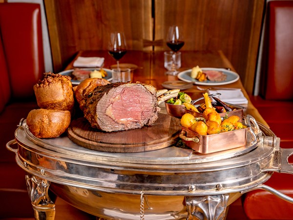 The Connaught Grill Sunday Roast with meat being cut and assortment of side dishes on a table.