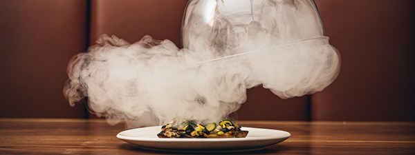 A white plate with a colourful dish in it, with smoke around it.