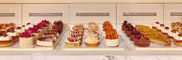 A display of intricate pastries and desserts in a refrigerated glass case, each with delicate toppings and vibrant colours.